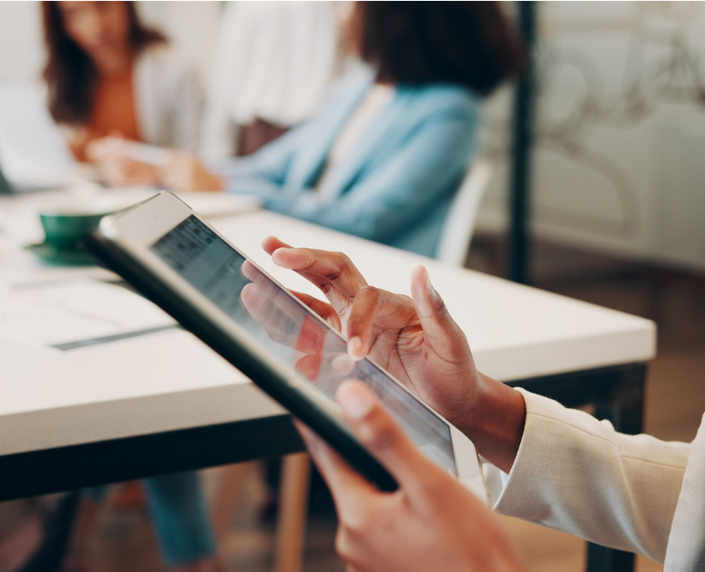 Person holding a tablet while standing in a room where people are talking